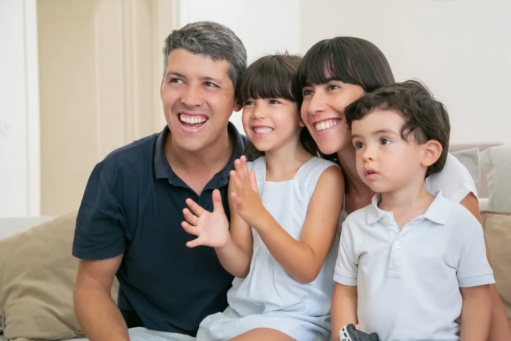 Eltern mit zwei Kindern sitzen lächelnd auf dem Sofa vor dem Fernseher